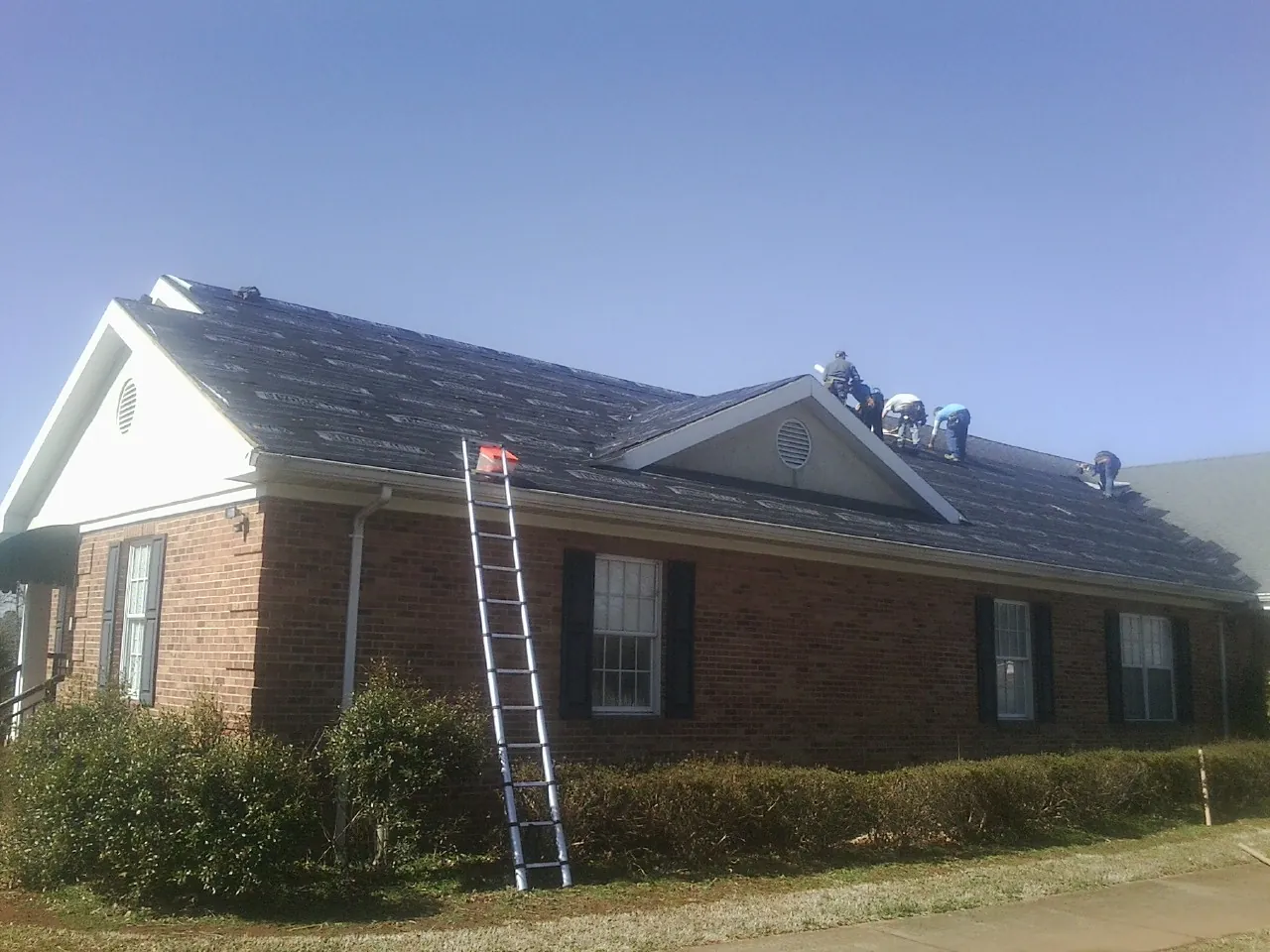 Crew tearing shingles off a brick ranch roof with a ladder set — Metal Roof Repair work by our crew in Ridge Spring