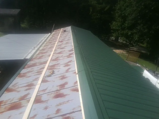 Old rusted panels beside newly installed green metal roofing — Wind Damage Roof Repair by Roofing Brothers in Ridge Spring