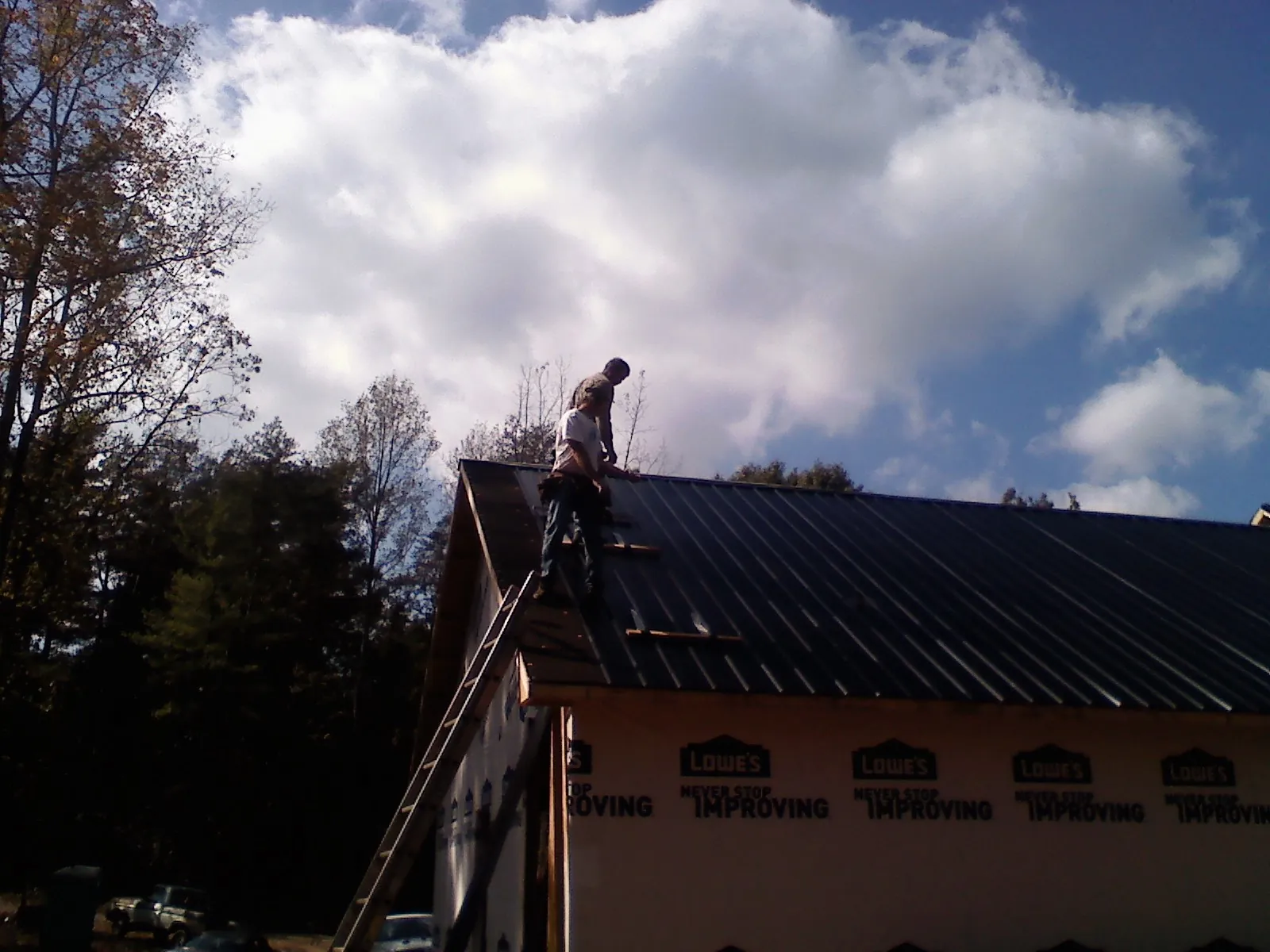 Roofer fastening dark metal panels high against a cloudy sky, from a Roof Inspection job in Ridge Spring